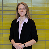 Olivia Goosen standing in front of yellow tiled wall, wearing black suit
